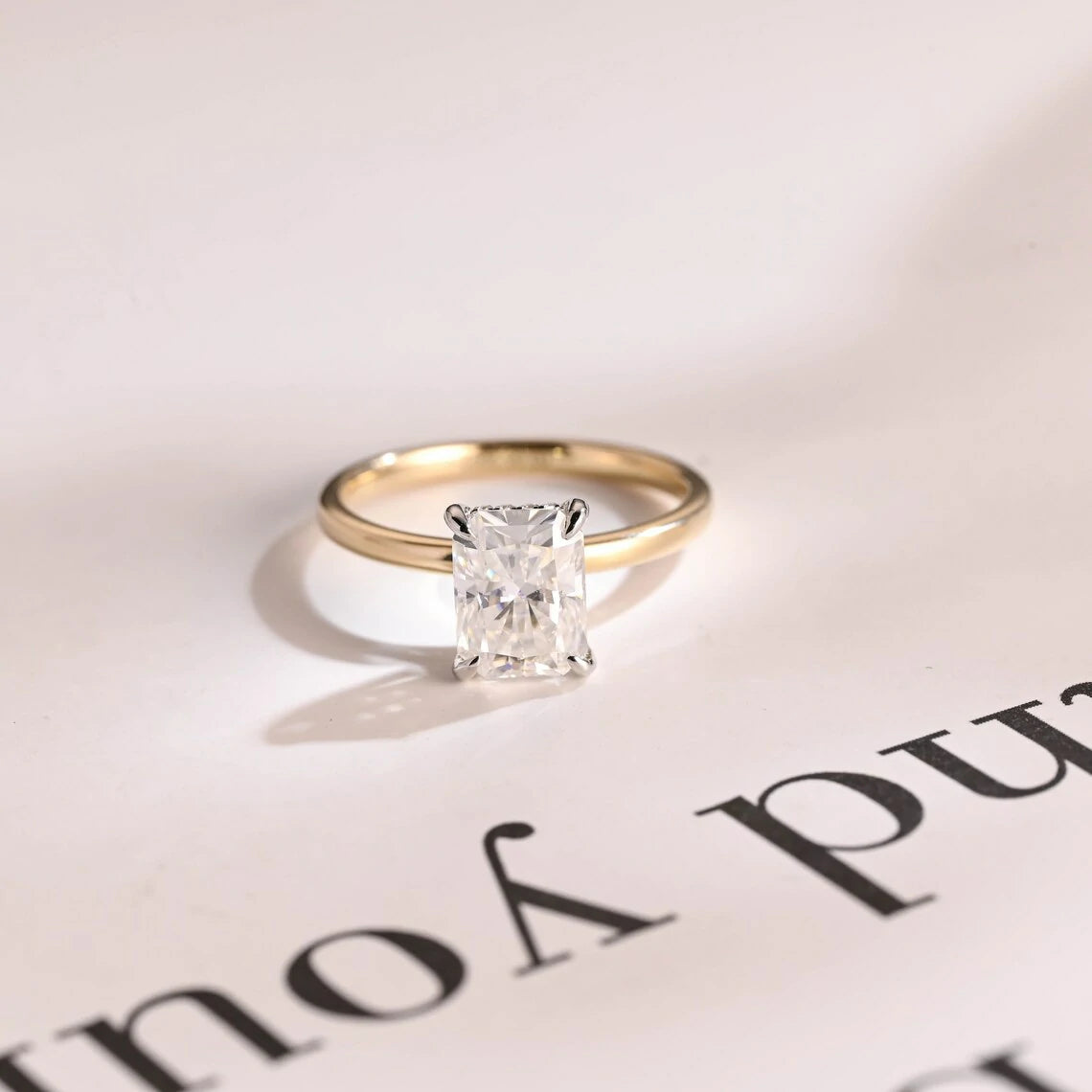 Stunning moissanite solitaire ring with radiant cut stone in yellow gold. Features a hidden halo for subtle glam and brilliant shine.