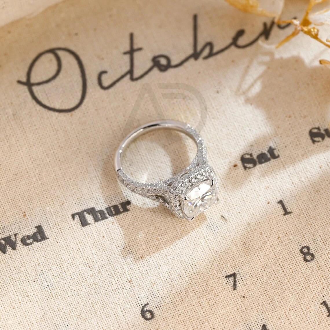 Vintage Cushion Cut Split Shank Moissanite Engagement Ring. This ring features a dazzling 3CT cushion cut moissanite diamond adorned with a halo design. Shop now!