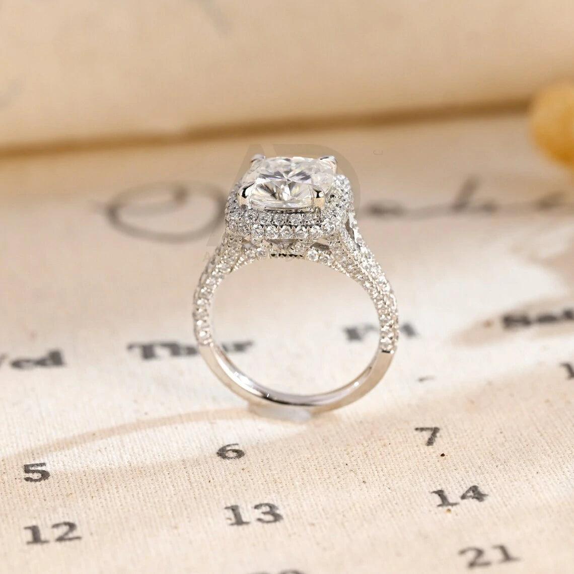 Vintage Cushion Cut Split Shank Moissanite Engagement Ring. This ring features a dazzling 3CT cushion cut moissanite diamond adorned with a halo design. Shop now!