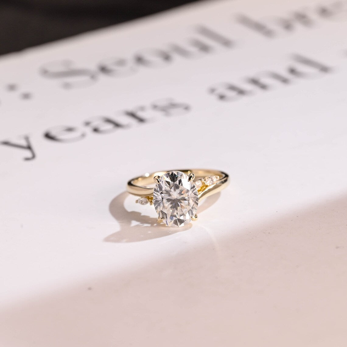Oval moissanite engagement ring in yellow gold with side accent diamonds. A timeless, elegant, handmade bridal ring perfect for proposals and meaningful gifting.