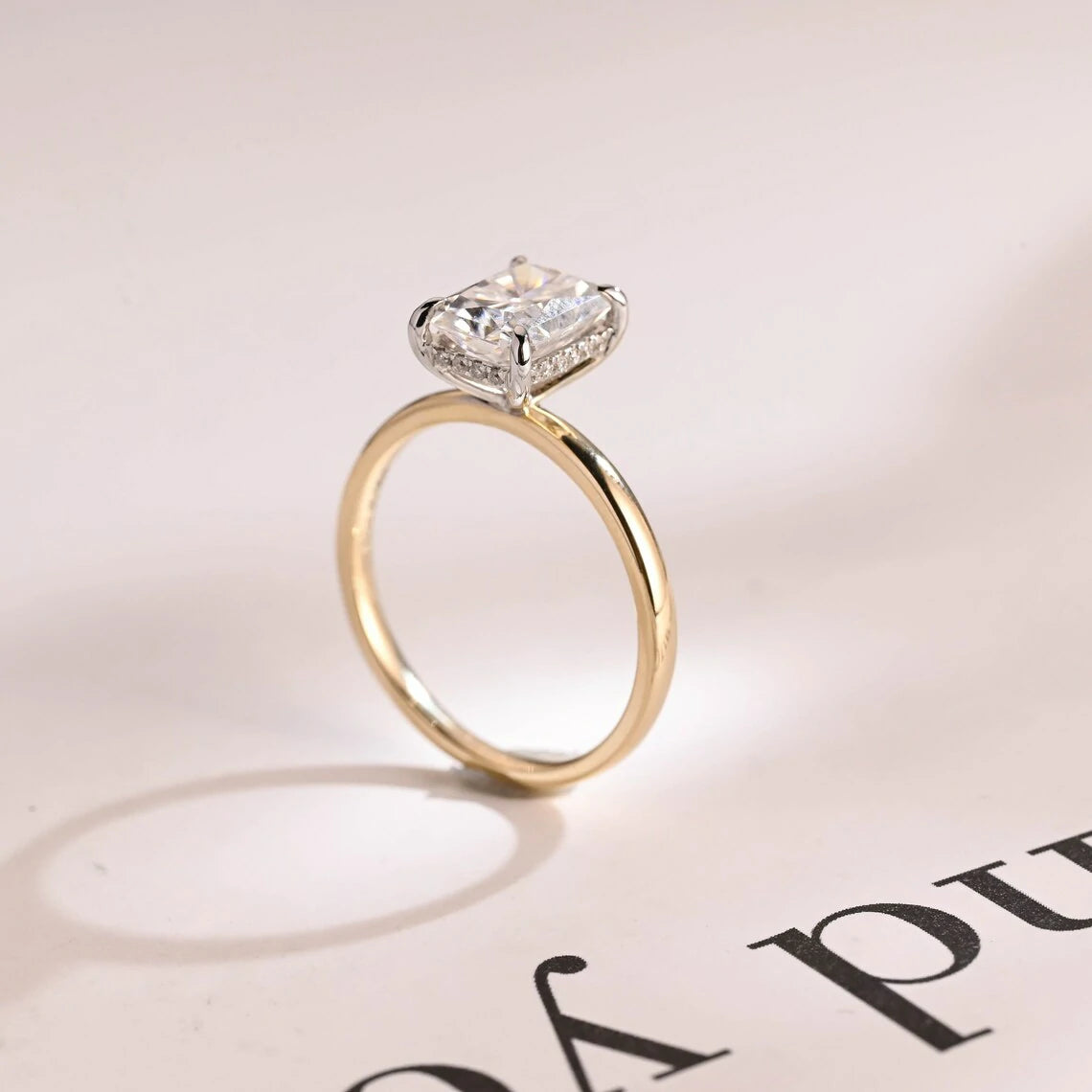 Stunning moissanite solitaire ring with radiant cut stone in yellow gold. Features a hidden halo for subtle glam and brilliant shine.