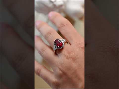 Oval cut red ruby engagement ring with cubic zirconia diamond halo and round side stones. cluster accent ring perfect for proposals, anniversary bridal jewelry.
